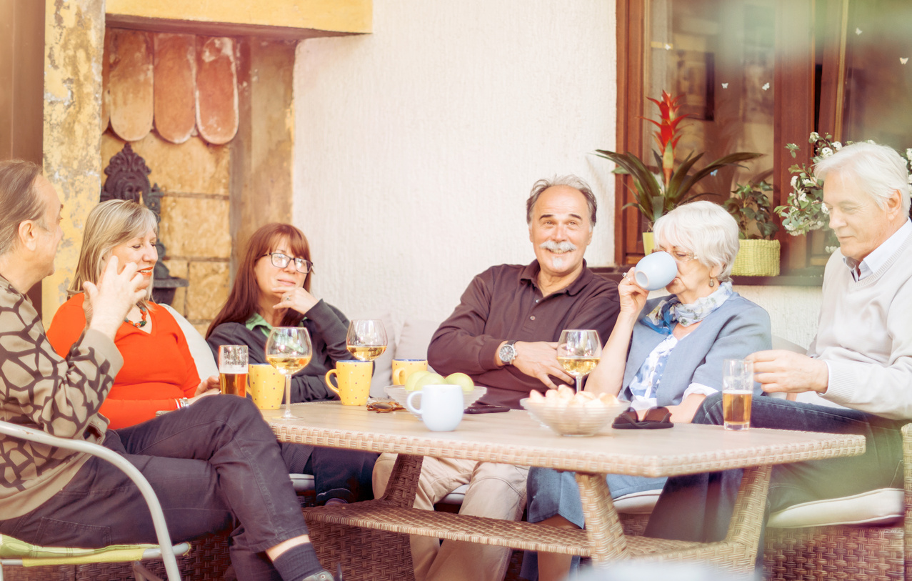 Middle age and older adults sitting around table smiling, drinking coffee.